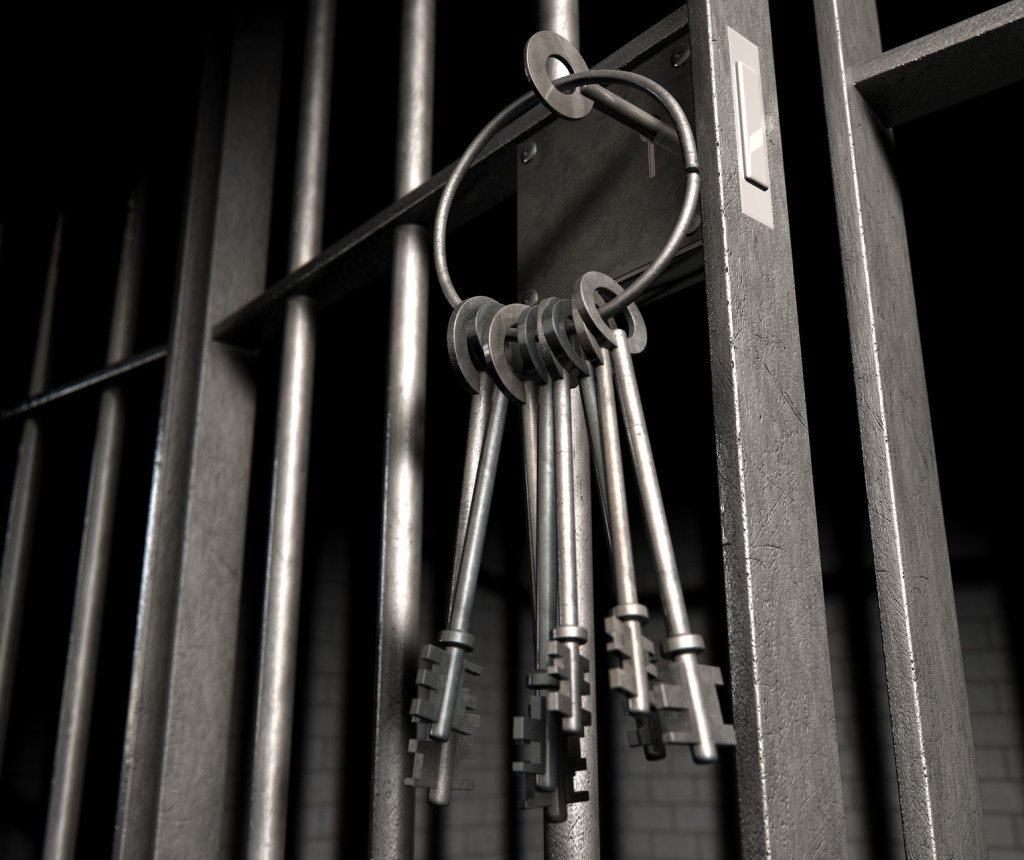 A closeup of the lock of a  jail cell with iron bars and a bunch of key in the locking mechanism with the door open